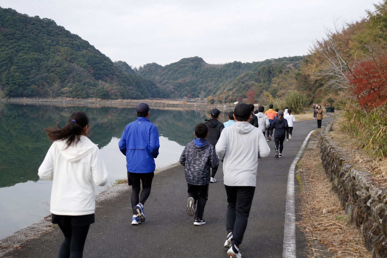 晩秋の湖畔の道を、後ろ姿でゆっくり走るランナーたちのイメージ