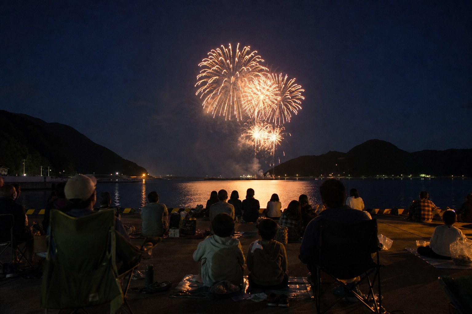 夜の漁港で花火を見上げる人たちのイメージ