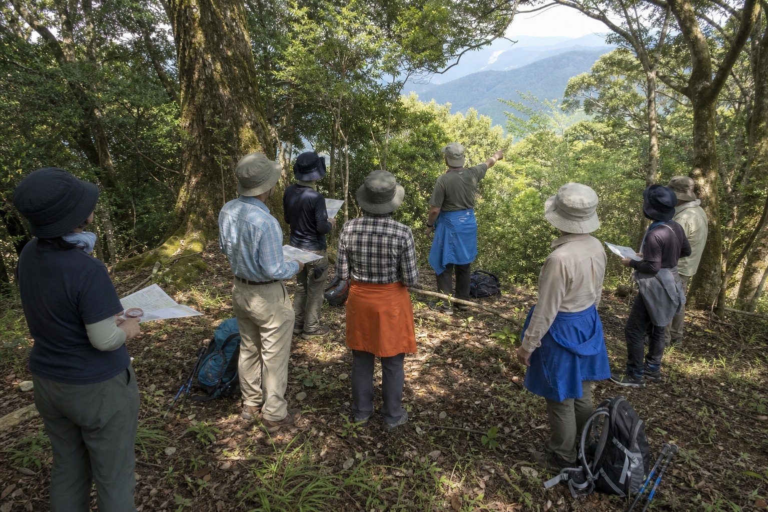 山の中腹で地図とコンパスを手に、講師から読図を教わる登山講座の参加者たち